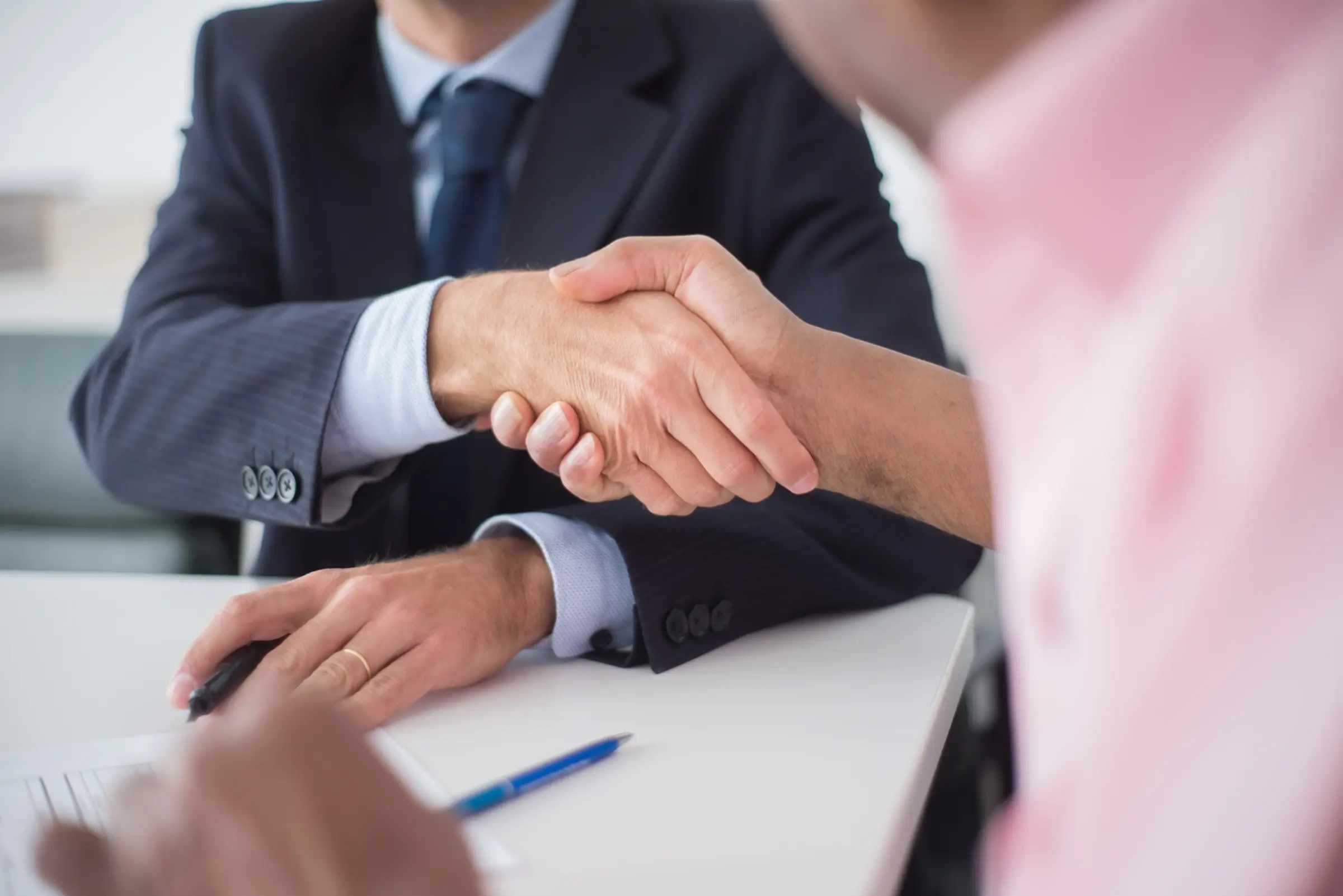 Two people shaking hands across a desk over a signed document