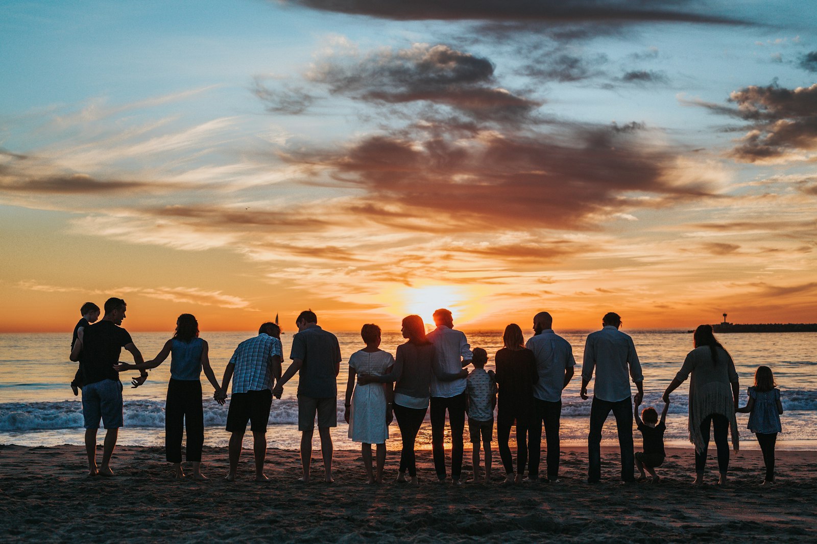 Extended family holding hands on a beach at sunset